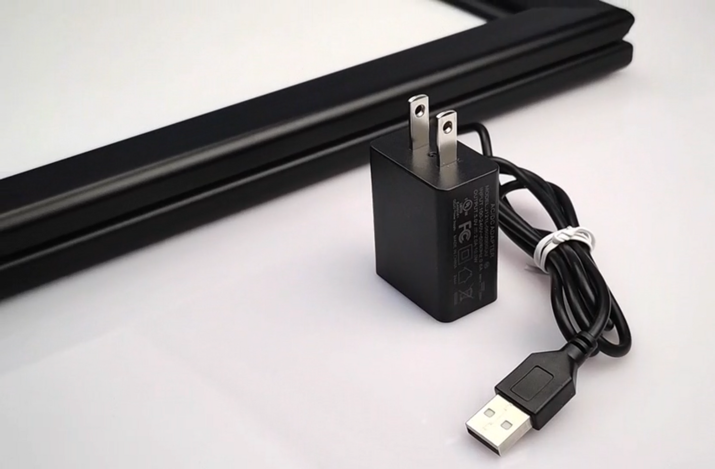 6ft USB power cable and included wall adapter shown next to the corner of the RGB LED acrylic lightbox frame, demonstrating the standard plug-and-play setup for Snapping Turtle Gallery frames.