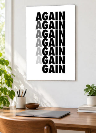 Again Becomes Gain acrylic wall art displayed above a wooden desk with a laptop, plants and books against a white wall.