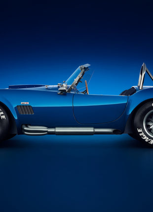 Blue open roadster in left-facing side profile with a chrome exhaust, rollover hoop, and white tire lettering against a navy studio glow; Cobalt Afterglow artwork