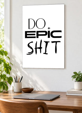 Do Epic Shit acrylic wall art displayed above a wooden desk with a laptop, plants and books against a white wall.
