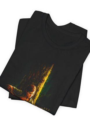 Folded black T-shirt close-up showing Ellie’s downturned face, tattooed forearm and the upper edge of her guitar beneath a golden-lit tree trunk.