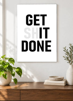 Get It Done acrylic wall art displayed above a wooden console with plants and books against a white wall.