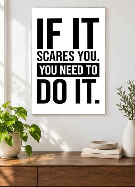 If It Scares You acrylic wall art displayed above a wooden console with plants and books against a white wall.