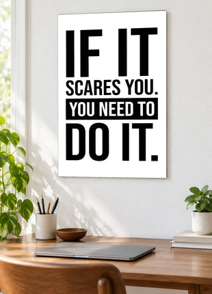 If It Scares You acrylic wall art displayed above a wooden desk with a laptop, plants and books against a white wall.