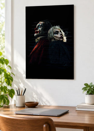 Joker and Harley Back to Back acrylic wall art displayed above a wooden desk with a laptop, plants and books against a white wall.