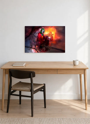 Joker Cart Full of Chaos acrylic wall art displayed above a wooden desk with a notebook, pencil and white mug against a white wall.