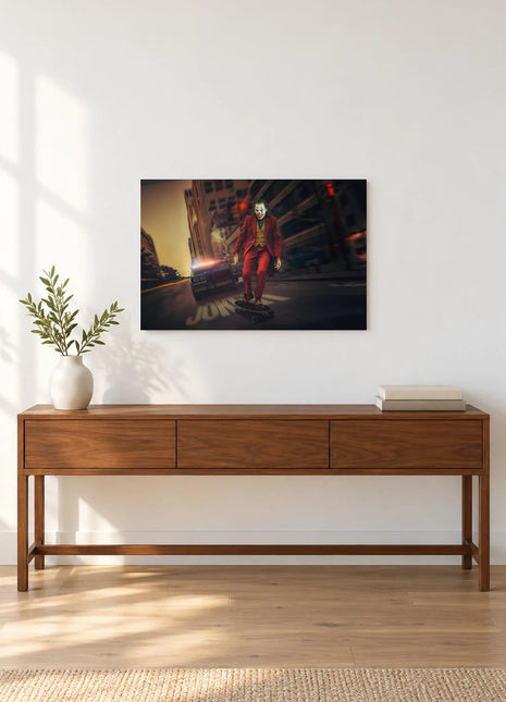 Joker Wheels of Mischief acrylic wall art displayed above a wooden console with a leafy vase and stacked books against a white wall.