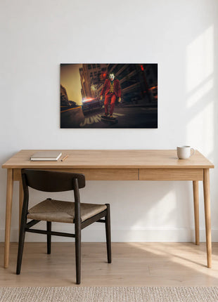 Joker Wheels of Mischief acrylic wall art displayed above a wooden desk with a notebook, pencil and white mug against a white wall.
