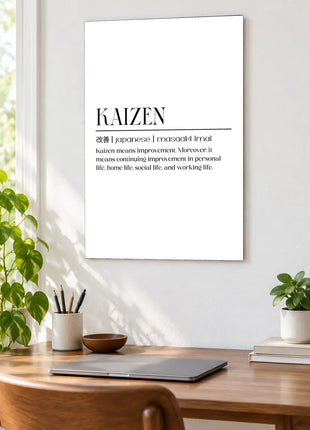 Kaizen Defined acrylic wall art displayed above a wooden desk with a laptop, plants and books against a white wall.