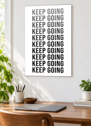 Keep Going in Full Focus acrylic wall art displayed above a wooden desk with a laptop, plants and books against a white wall.