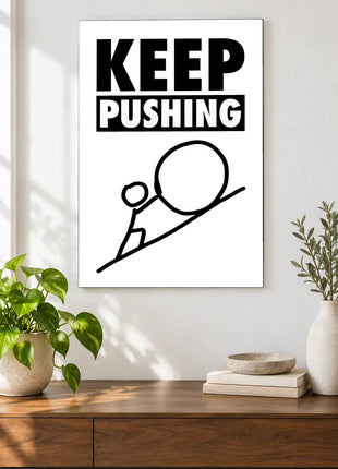 Keep Pushing Uphill acrylic wall art displayed above a wooden console with plants and books against a white wall.