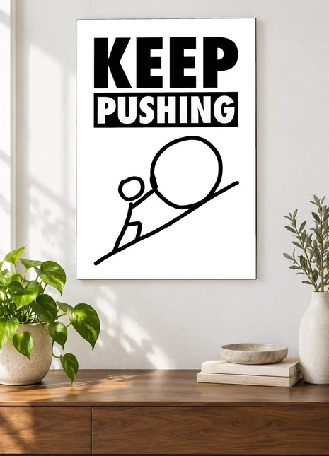 Keep Pushing Uphill acrylic wall art displayed above a wooden console with plants and books against a white wall.