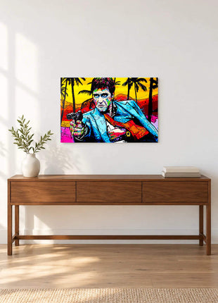 Tony Montana aiming a handgun in a blue jacket against bright palms and yellow sky displayed above a console table in a room setting