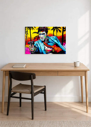 Tony Montana aiming a handgun in a blue jacket against bright palms and yellow sky displayed above a desk in a room setting