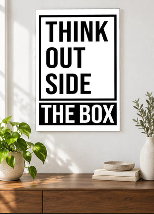 Outside the Box acrylic wall art displayed above a wooden console with plants and books against a white wall.