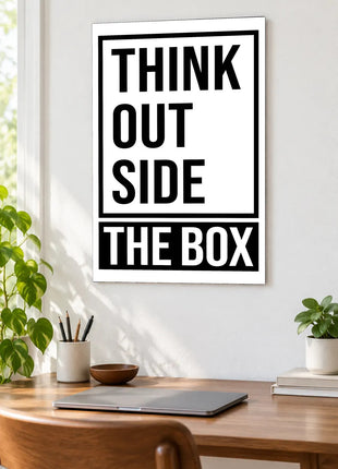 Outside the Box acrylic wall art displayed above a wooden desk with a laptop, plants and books against a white wall.