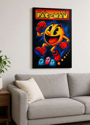 Pac-Man wearing red gloves and boots above three small ghosts, with arcade lettering across the top on acrylic wall art above a light gray sofa in a living room with white walls.