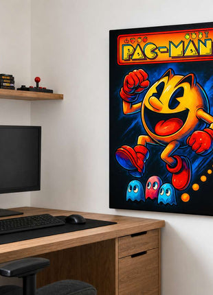 Pac-Man wearing red gloves and boots above three small ghosts, with arcade lettering across the top on canvas wall art beside a computer monitor and oak desk in a game room with white walls.