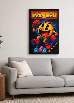 Pac-Man wearing red gloves and boots above three small ghosts, with arcade lettering across the top on canvas wall art above a light gray sofa in a living room with white walls.