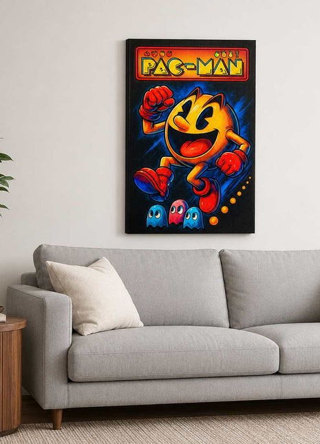 Pac-Man wearing red gloves and boots above three small ghosts, with arcade lettering across the top on canvas wall art above a light gray sofa in a living room with white walls.