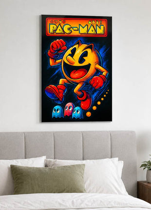 Pac-Man wearing red gloves and boots above three small ghosts, with arcade lettering across the top on metal wall art above a gray upholstered headboard in a bedroom with white bedding.