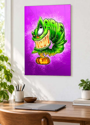Green toothy cartoon monster above a jack-o'-lantern on purple and magenta displayed above a desk in a room setting
