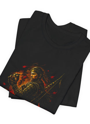 Folded black T-shirt close-up showing the samurai’s headband, layered armor and hands holding an owl-shaped figure.