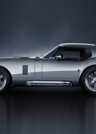 Silver long-nose racing coupe facing left in side profile, with a fastback roof, rear lip spoiler and side exhaust over a gray reflection.