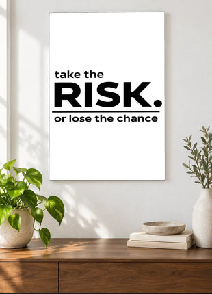 Take the Risk acrylic wall art displayed above a wooden console with plants and books against a white wall.