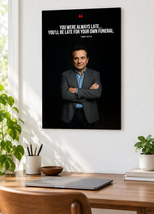 Tommy DeVito Late Arrival acrylic wall art displayed above a wooden desk with a laptop, plants and books against a white wall.
