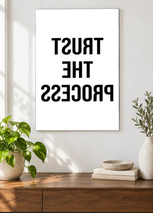 Trust the Process in Reverse acrylic wall art displayed above a wooden console with plants and books against a white wall.