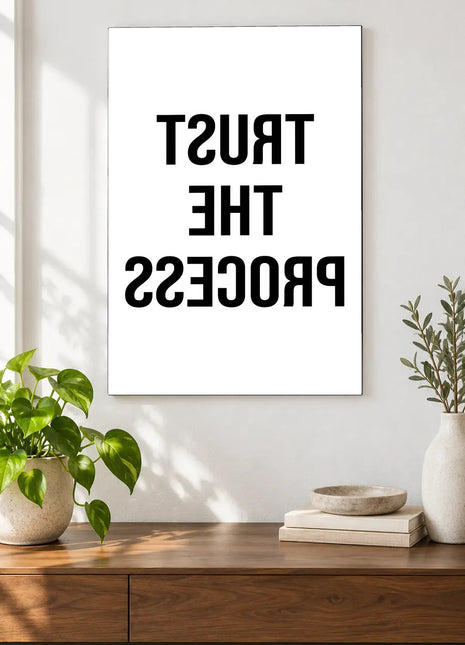 Trust the Process in Reverse acrylic wall art displayed above a wooden console with plants and books against a white wall.