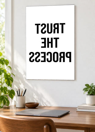 Trust the Process in Reverse acrylic wall art displayed above a wooden desk with a laptop, plants and books against a white wall.