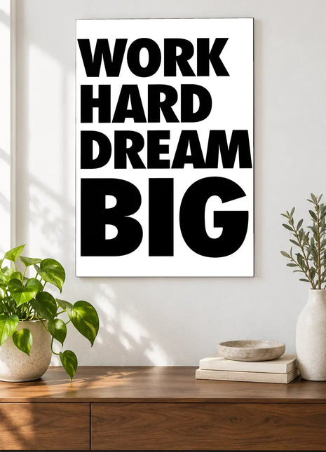Work Hard Dream Big acrylic wall art displayed above a wooden console with plants and books against a white wall.
