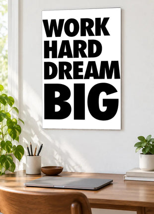 Work Hard Dream Big acrylic wall art displayed above a wooden desk with a laptop, plants and books against a white wall.